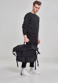 Sort rygsæk med dobbelt topgreb, flere lommer, justerbare stropper og et slankt, struktureret design. Fremstillet af slidstærkt stof.