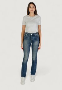 Camiseta gris con cuello adornado, combinada con unos vaqueros ajustados azul y zapatillas blancas. Los vaqueros presentan un diseño clásico de pierna recta.