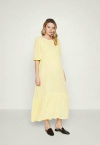 Vestido amarelo, até ao joelho, com decote quadrado, mangas curtas em forma de balão e bainha em camadas com volantes. Tecido suave e corte descontraído.