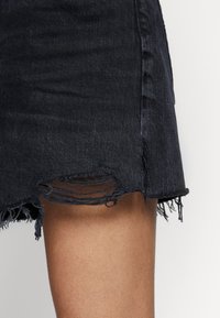 Falda de mezclilla en tono oscuro con dobladillo deshilachado y detalles desgastados. Presenta un diseño ajustado y una textura sutil acorde con la tela de mezclilla.