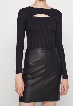 Zwart geribd top met lange mouwen en een uitgesneden halslijn, gecombineerd met een aansluitende zwarte leren minirok. Gladde textuur met een strak ontwerp.