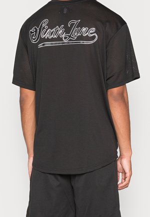 Persona che indossa una maglia nera a maniche corte in rete e pantaloncini abbinati con la scritta "Sixth June" in bianco sulla schiena della maglia.