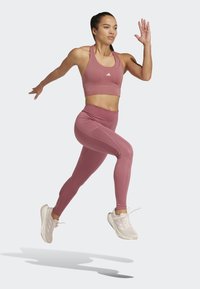 Top corto atlético rosa y leggings de cintura alta a juego, hechos de material elástico, combinados con zapatillas de correr de color claro.