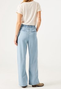 Jeans de pierna ancha de color azul claro con cintura elástica y dos bolsillos traseros, combinados con una camiseta de manga corta beige.