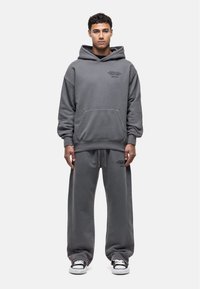 Gray hoodie and sweatpants set made of soft fabric. Hoodie has a front pocket and printed text; pants feature an elastic waistband.