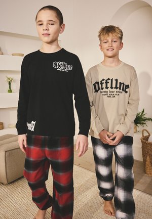 Két fiú hosszú ujjú „offline” pólót és kockás pizsamát visel, mezítláb állnak egy hangulatos nappaliban.