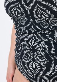 Sort mønstret badedragt med hvide blomster motiver. Stoffet har en struktureret overflade med rynkede detaljer langs siderne.
