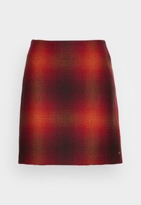 Punaiset ja tumman oranssit ruudulliset minihameet, joissa on hienovarainen värigradientti ja pieni metallilogo alahelman lähellä.