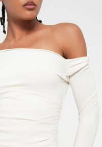 Bela bluzica brez naramnic iz raztegljive tkanine, z dolgimi rokavi z nabiranjem, gladko teksturo in oprijetim krojem.