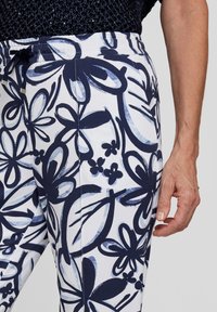 Floral-patterned pants in white with navy blue and light blue designs. Features an elastic waistband and a relaxed fit with a drawstring.