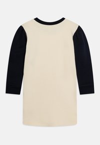 Helles beige Baumwollkleid mit dunkelblauen langen Ärmeln und rundem Hals. Glatte Textur, schlichtes Design und kontrastierende Farbstreifen.