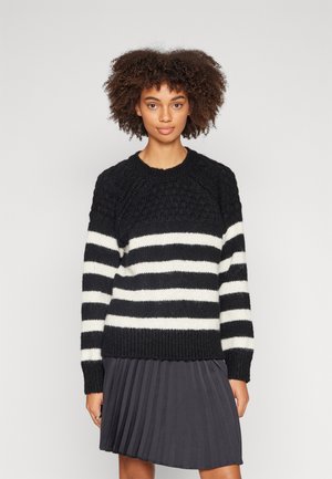 Black and white striped sweater with a textured yoke, ribbed cuffs, and hem. Paired with a pleated dark skirt.