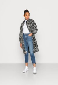 Casaco com padrão de leopardo em cinza e preto, apresentando fechamento com botões, combinado com jeans rasgados e ténis brancos.