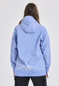 Himmelblaues Kapuzenshirt aus weichem Stoff, mit einer Fronttasche, verstellbarer Kapuze und Logo auf der Rückseite. Enthält seitliche Reißverschlüsse für zusätzliche Details.