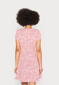 Rood en wit gestippeld jurkje met korte mouwen, aansluitende lijfje en uitlopende zoom. Lichtgewicht stof, gladde textuur en eenvoudige ronde halslijn.