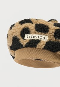 Καπέλο με λεοπάρ σχέδιο σε καφέ και μαύρο, κατασκευασμένο από απαλό υλικό με ριγωτή μπεζ πλέξη. Διαθέτει ορθογώνια ετικέτα με το όνομα της μάρκας.