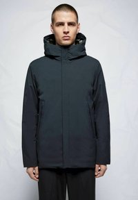 Chaqueta azul marino oscura con cuello alto y capucha, que presenta bolsillos delanteros con cremallera y una textura mate y suave. Diseño minimalista.