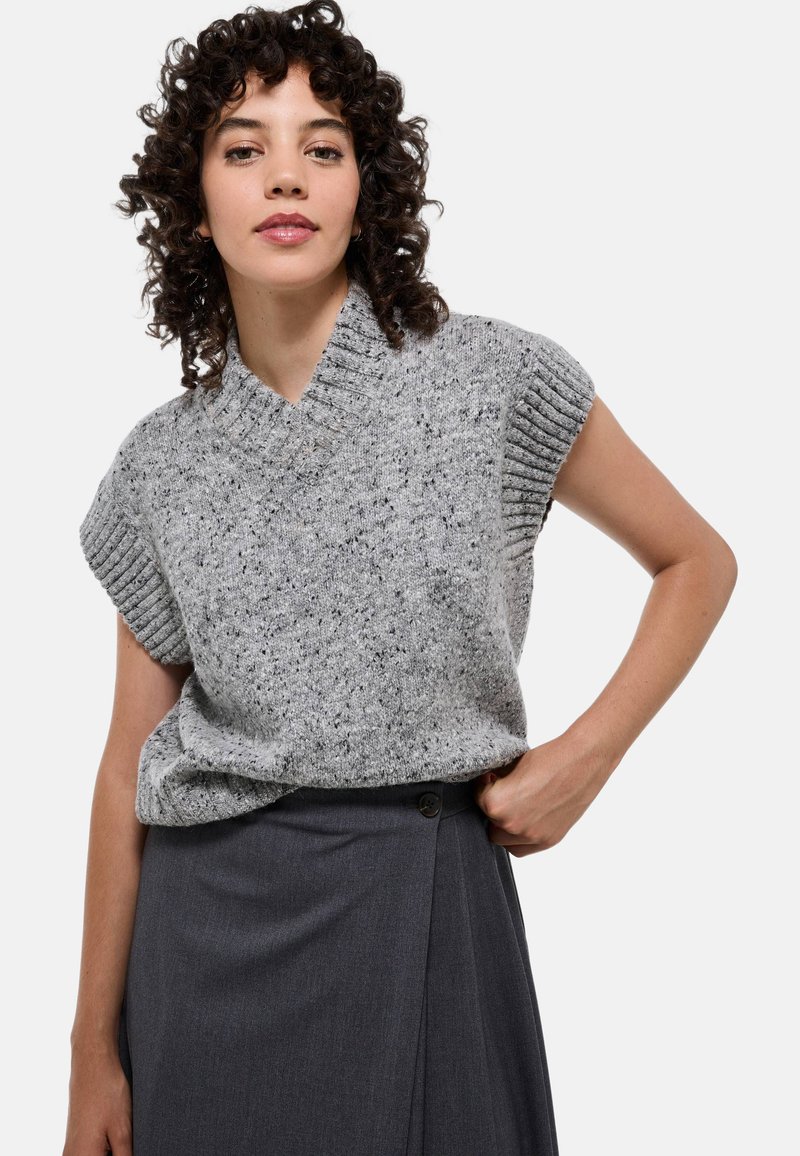 Pull en tricot gris à manches courtes avec un col en V et des bords côtelés, associé à une jupe portefeuille gris foncé, dotée d'un détail de bouton.