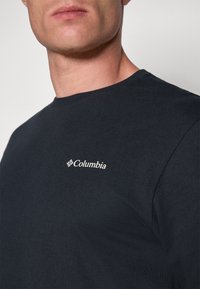 T-shirt en coton bleu marine avec un col rond et un petit logo blanc Columbia sur le côté supérieur gauche. Texture lisse et design simple.