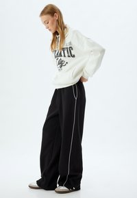 Witte fleecetrui met zwart grafisch ontwerp, gecombineerd met zwarte wijde sweatpants met witte zijnaad en eenvoudige sneakers.