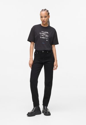 Zwarte katoenen T-shirt met korte mouwen, voorzien van witte tekstgrafiek. Gecombineerd met hoog-waist zwarte jeans en stevige zwarte laarzen.