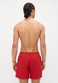 Shorts de bain rouges en tissu léger, dotés d'une taille élastique et d'un design simple sans logos ni motifs visibles.