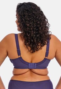 Paarse nylon bh met verstelbare bandjes, gestructureerde, gegolfde randen en een rugsluiting met drie haakjes. Heeft een glad, gevormd ontwerp.