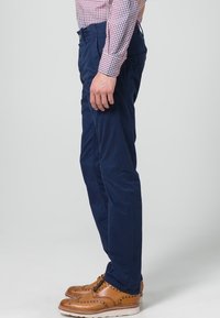 Námořnicky modré úzké kalhoty z bavlny s bočními kapsami a hladkým povrchem, doplněné o hnědé brogue boty.