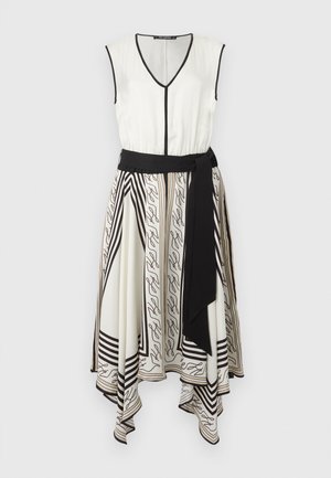 Ermeløs hvit kjole med svart kant, V-hals, asymmetrisk kant, mønstrede skjørtpaneler, og et bredt svart midjebelte.