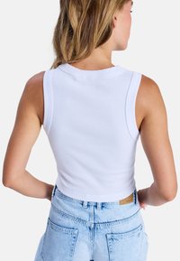 Witte geribbelde crop top met een ronde halslijn, mouwloos ontwerp en een getailleerde pasvorm, gecombineerd met hoge taille lichtblauwe spijkerbroek.