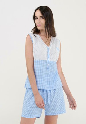 Mujer con top sin mangas de patrón vichy azul y blanco y shorts a juego, de pie contra un fondo claro y liso.