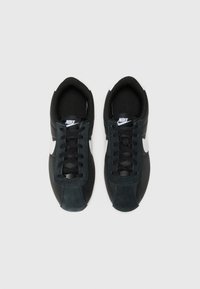 Crne Nike tenisice s kombinacijom kože i antilopa. Imaju bijeli Swoosh, zaobljeni vrh i crne vezice. Strukturirana gornja površina.