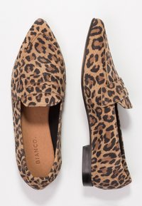 Une paire de mocassins à bout pointu pour femmes avec un imprimé léopard brun et noir et des talons plats noirs sur fond blanc.