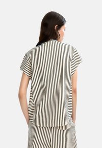Stripet topp laget av lett stoff, med korte ermer, avrundet hem og marineblå striper på en off-white bakgrunn.