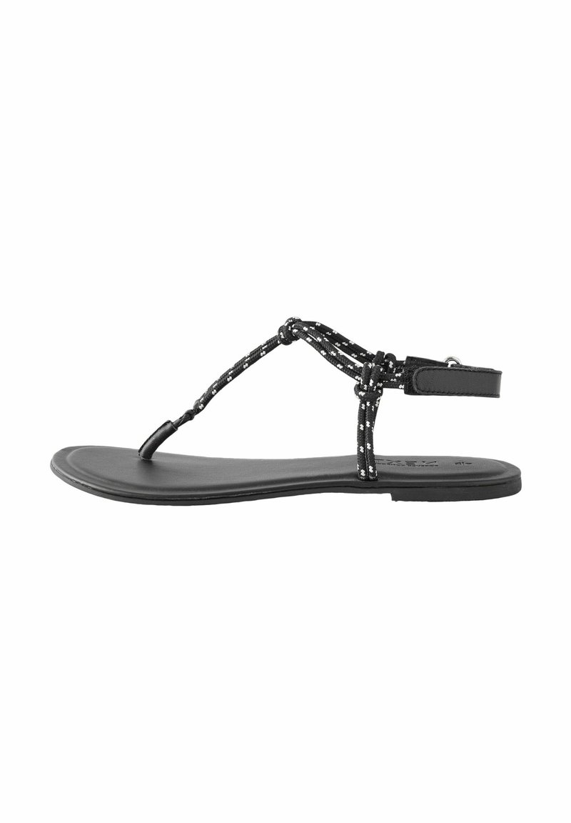 Black flat sandal with a T-strap design, featuring braided black and white cords and an adjustable ankle strap. Smooth sole and minimal profile.