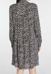 Abito a maniche lunghe con un motivo astratto in bianco e nero, realizzato in tessuto leggero con vita arricciata e gonna fluida.