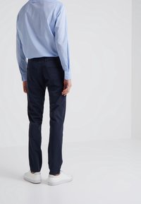 Námořnické bavlněné kalhoty slim fit, s kapsami na zadní straně, v kombinaci se světle modrou košilí na knoflíky a bílými teniskami.