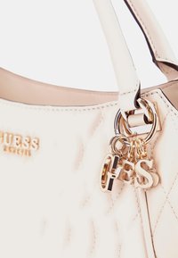 Borsa a tracolla color crema trapuntata con logo "GUESS" in metallo dorato e charm a lettere appesi all'anello della maniglia.
