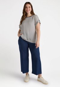 Kurzärmlige, gemusterte Bluse in Creme und Marineblau, kombiniert mit dunkelblauen, weit geschnittenen Hosen und beigen Sneakers. Lässiger, lockerer Schnitt.