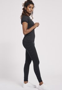 Svart träningstopp och leggings, båda figurnära, med texturerade detaljer och chevronmönster. Vita sneakers kompletterar outfiten.