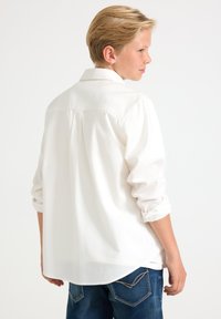 Hvid skjorte med knapper, krave, lange ærmer rullet ved manchetterne og en buet kant, kombineret med blå denimjeans.