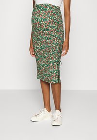 Green floral maternity skirt with a fitted design, gathered texture, and side slit, paired with white sneakers.