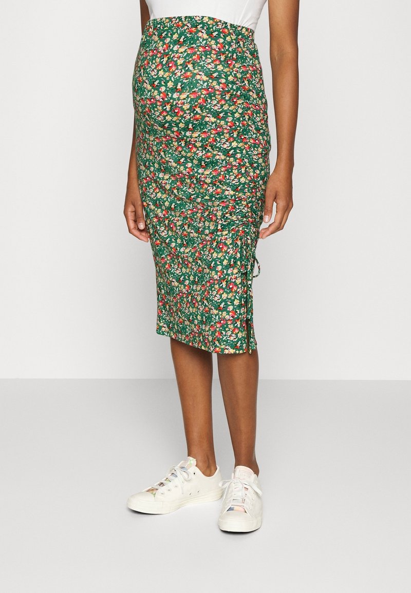 Green floral maternity skirt with a fitted design, gathered texture, and side slit, paired with white sneakers.
