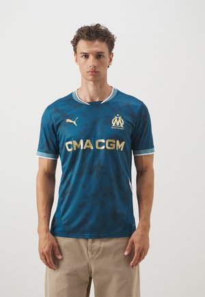Maglia sportiva blu con motivo, rifiniture bianche e dettagli dorati, dotata di un logo sul petto e testo dello sponsor. Realizzata in tessuto traspirante.
