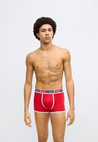 Sarkanas bokseršorti ar melnu elastīgu jostasvietu, uz kuras redzams "DIESEL" logotips, baltu apmali un cieši pieguļošu piegriezumu. Gluda kokvilnas materiāla.