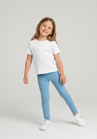 Biała koszulka z krótkim rękawem w połączeniu z jasnoniebieskimi legginsami i białymi trampkami. Strój jest dopasowany i wykonany z gładkiej tkaniny.