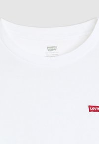 Biele bavlnené tričko s okrúhlym výstrihom. Na hrudi sa nachádza červená nálepka s logom Levi's, ktorá poskytuje jednoduchý a klasický dizajn.