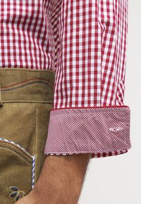 Chemise à carreaux vichy rouge et blanche avec poignet en tissu contrastant. Matière en coton avec une texture lisse. Présente un logo cousu sur le poignet.