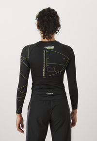 Svart langermet treningsskjorte med grønne geometriske design, merkelogo på kragen og baksiden, samt funksjonelt stoff for aktiv bruk.
