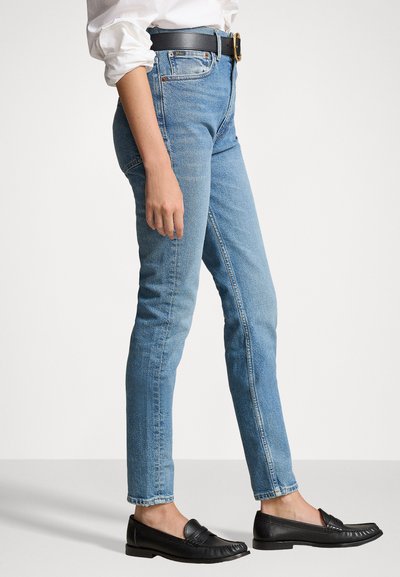 Blue denim jeans with a high waist, slim fit, and slight fading. Paired with black loafers and a black belt featuring a round buckle.